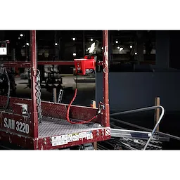 Locking Tool Lanyard attached to a red scaffolding platform in a dimly lit industrial setting.