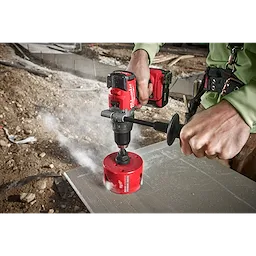 Person using a red cordless drill with 4-1/4" BIG HAWG with Carbide Teeth to drill through a concrete surface at a construction site.