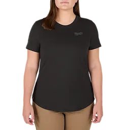 A woman is wearing the Women's FREEFLEX™ Hybrid Tee - Short Sleeve Black. The black tee has a round neckline and short sleeves, with the Milwaukee logo on the left chest. The woman is also wearing beige pants.