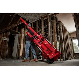 A person is pushing a red PACKOUT™ Tool Box with a Long Tool Holder Attachment through a construction site with exposed wooden beams. The tool box is stacked with other PACKOUT™ modules on a rolling cart.