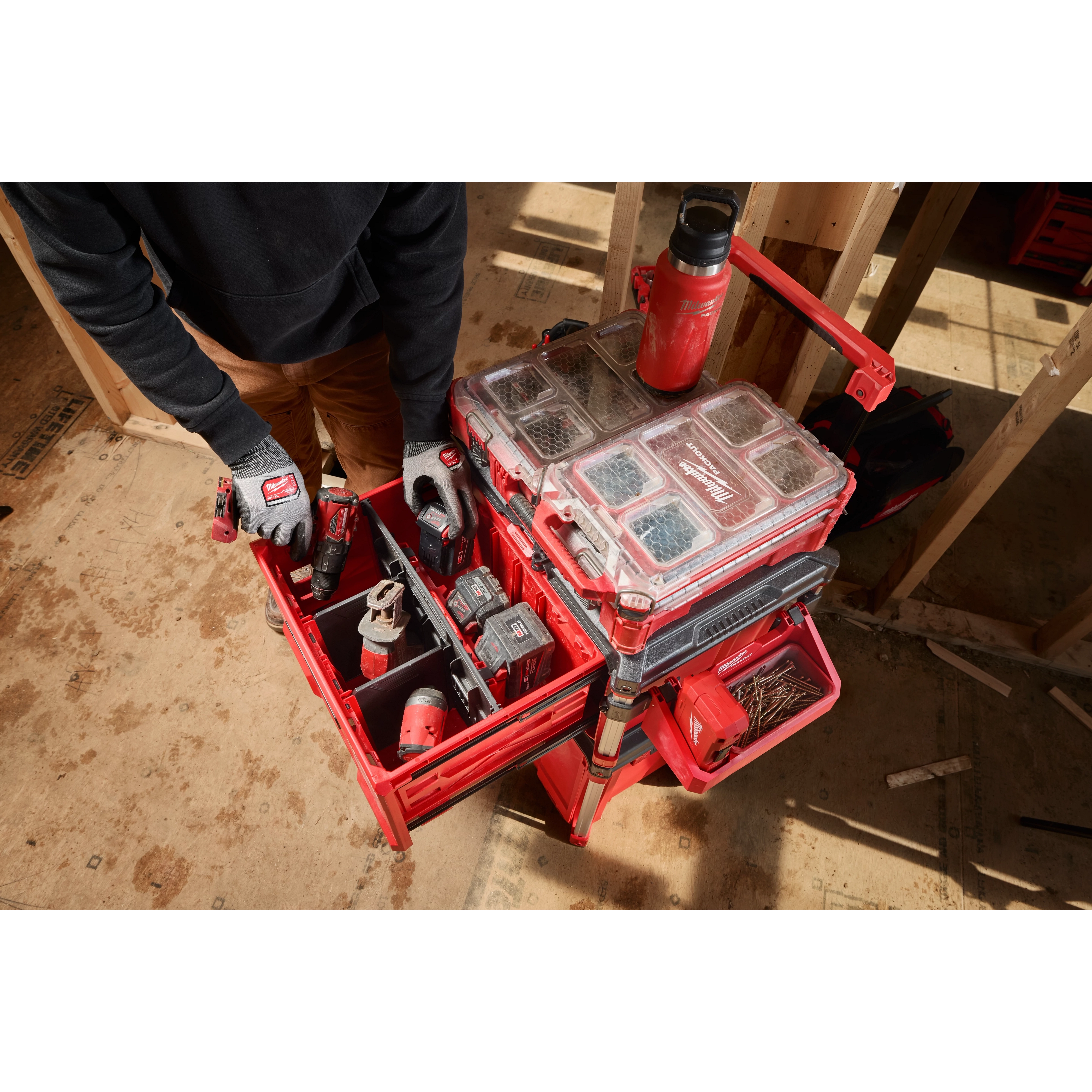 Worker accessing PACKOUT Single Drawer Tool Box stacked with organizers and tools on a construction site floor.