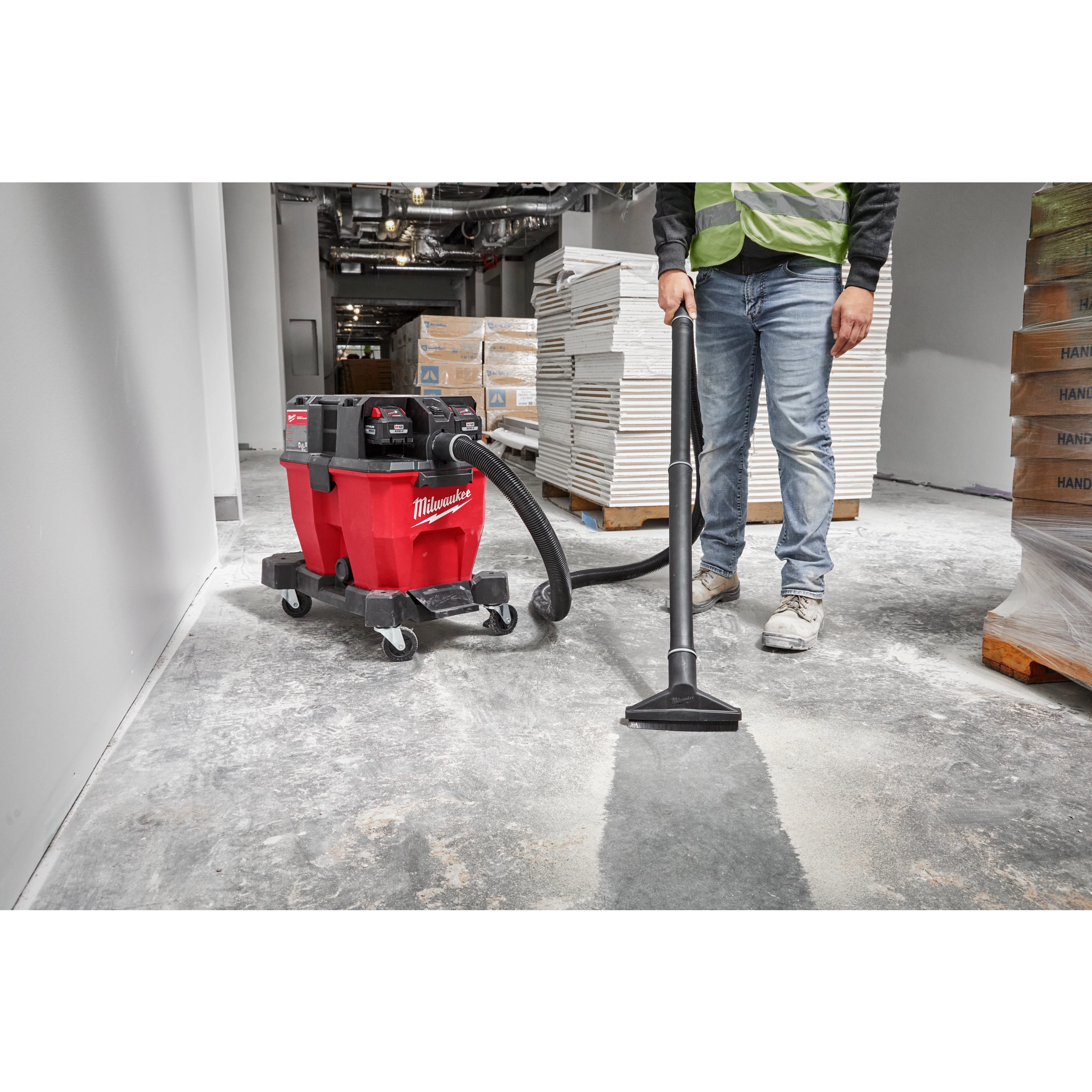 A worker uses the Milwaukee M18 FUEL 9 Gallon Dual-Battery Wet/Dry Vacuum to clean a construction site floor.