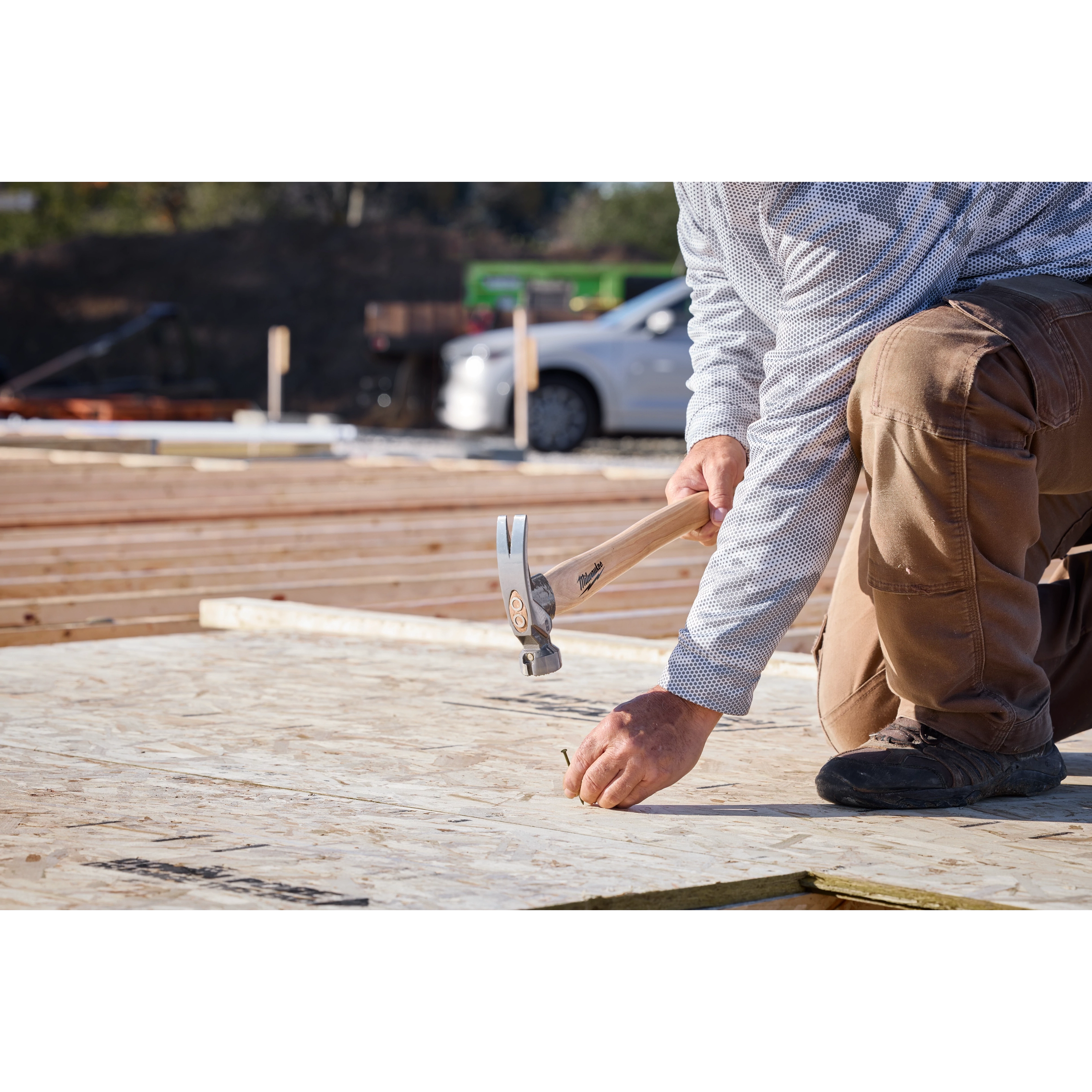 A worker nails plywood on a construction site using a 23oz Milled Face Hickory Handle Framing Hammer.