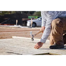 A worker nails plywood on a construction site using a 23oz Milled Face Hickory Handle Framing Hammer.