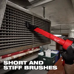 A person is using an AIR-TIP™ 3-in-1 Crevice and Brush Tool to clean the slats of a vent. The tool has a red handle and short, stiff brushes. The background includes industrial equipment and a caption reads "SHORT AND STIFF BRUSHES".