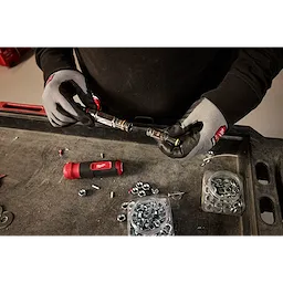 Person wearing protective gloves working with the 7-IN-1 HOLLOWCORE Multi-Nut Driver on a workbench with nuts, bolts, and components.