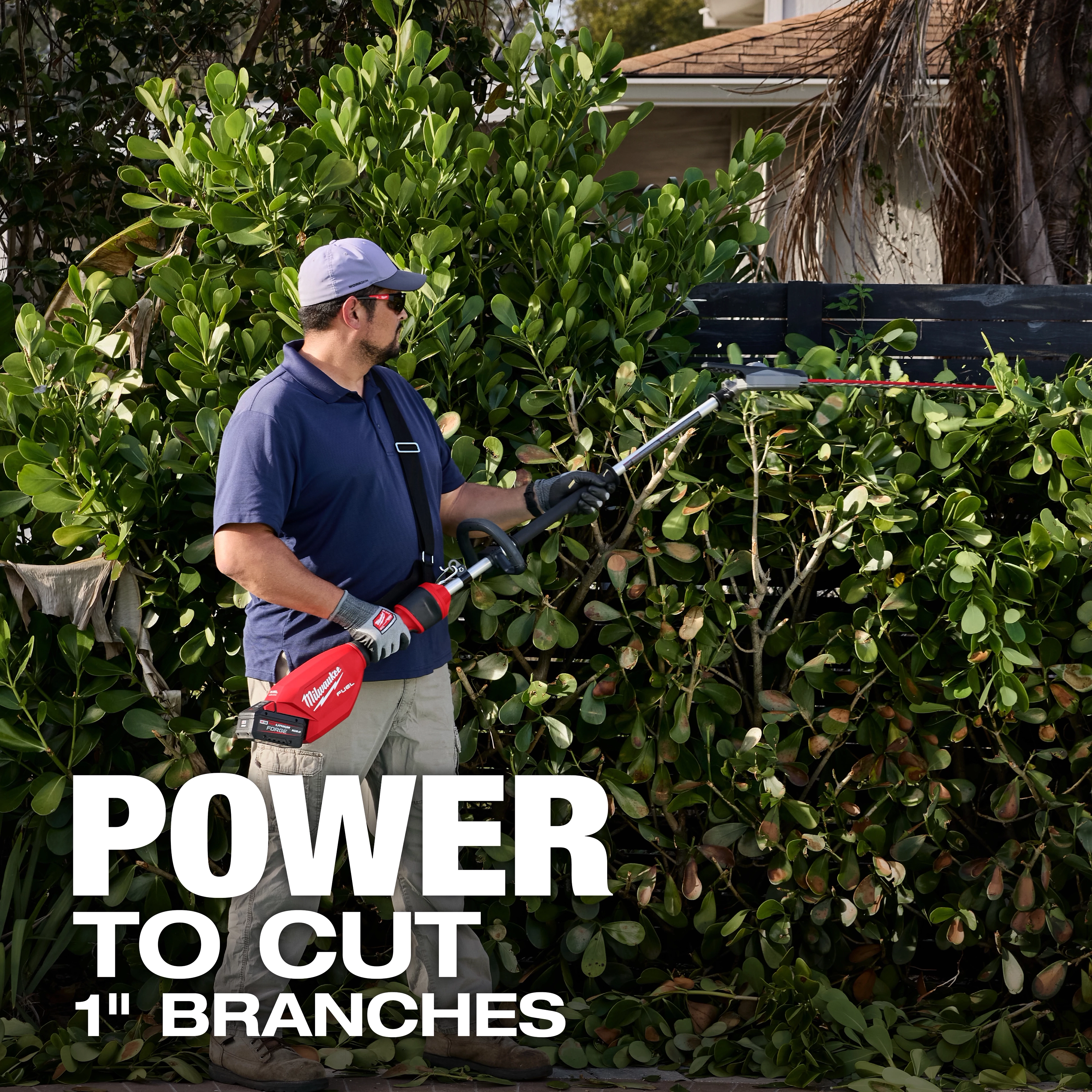 A man dressed in a blue polo shirt and khaki shorts trims a hedge with a red cordless pole saw. Text reads, "POWER TO CUT 1" BRANCHES." Dense foliage and a part of a house are in the background.