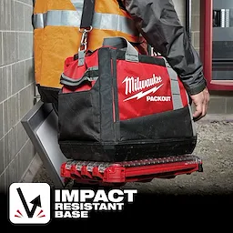 A person carries a Milwaukee Packout tool bag with App%20Shot%20Overlay, featuring an impact-resistant base, in a construction area.