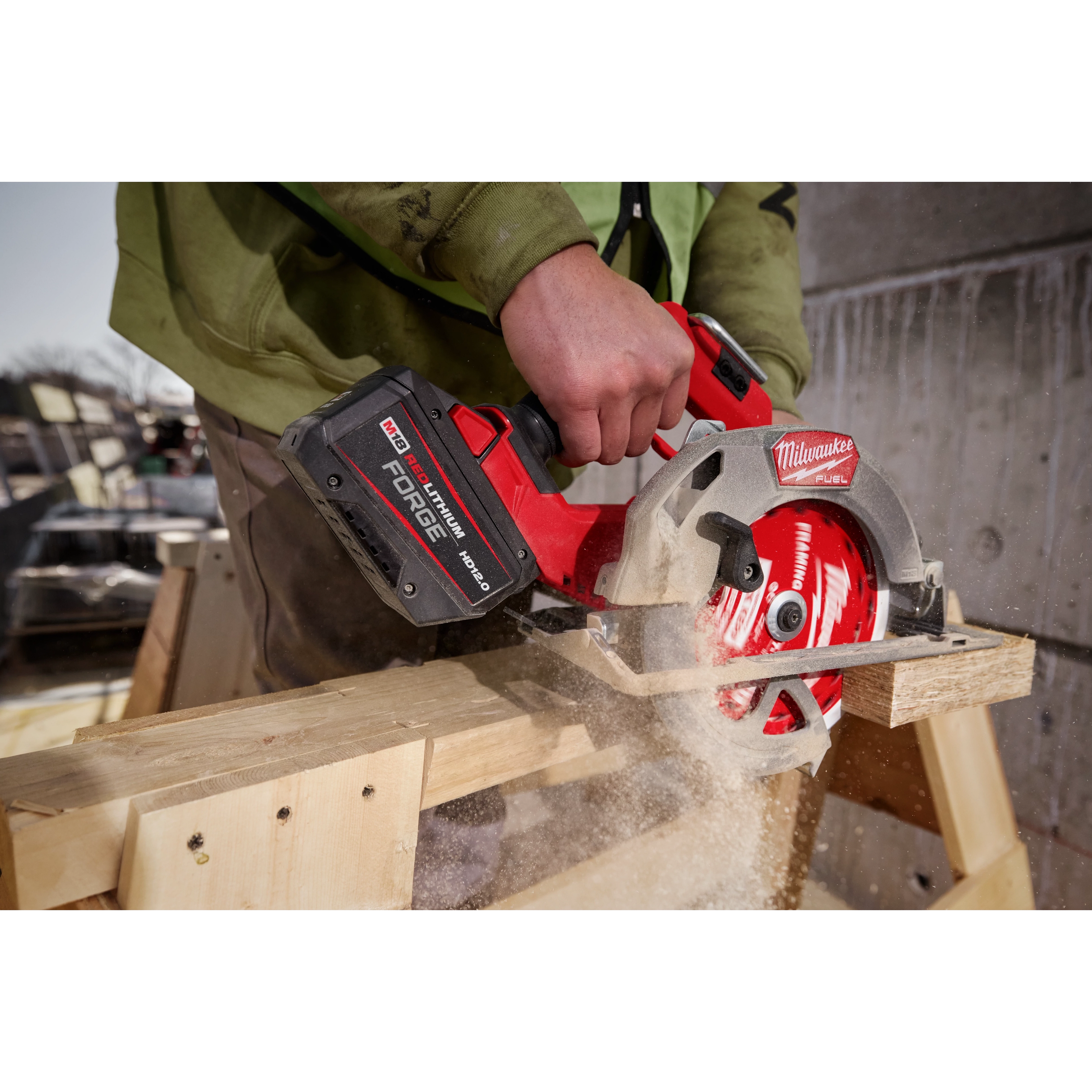 A person is using a power saw equipped with an M18™ REDLITHIUM™ FORGE™ HD12.0 Battery Pack to cut through a piece of wood. Dust and wood chips are seen from the cutting. The tool is being held firmly, and the scene appears to be an outdoor construction site.