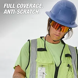 Worker wearing wrap-around safety glasses, a green safety vest with reflective strips, and a blue hard hat. The image has the text "Full Coverage. Anti-Scratch."