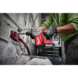 Person using a red M18 FUEL 1-1/8" SDS Plus Rotary Hammer to drill into a grey concrete block wall.