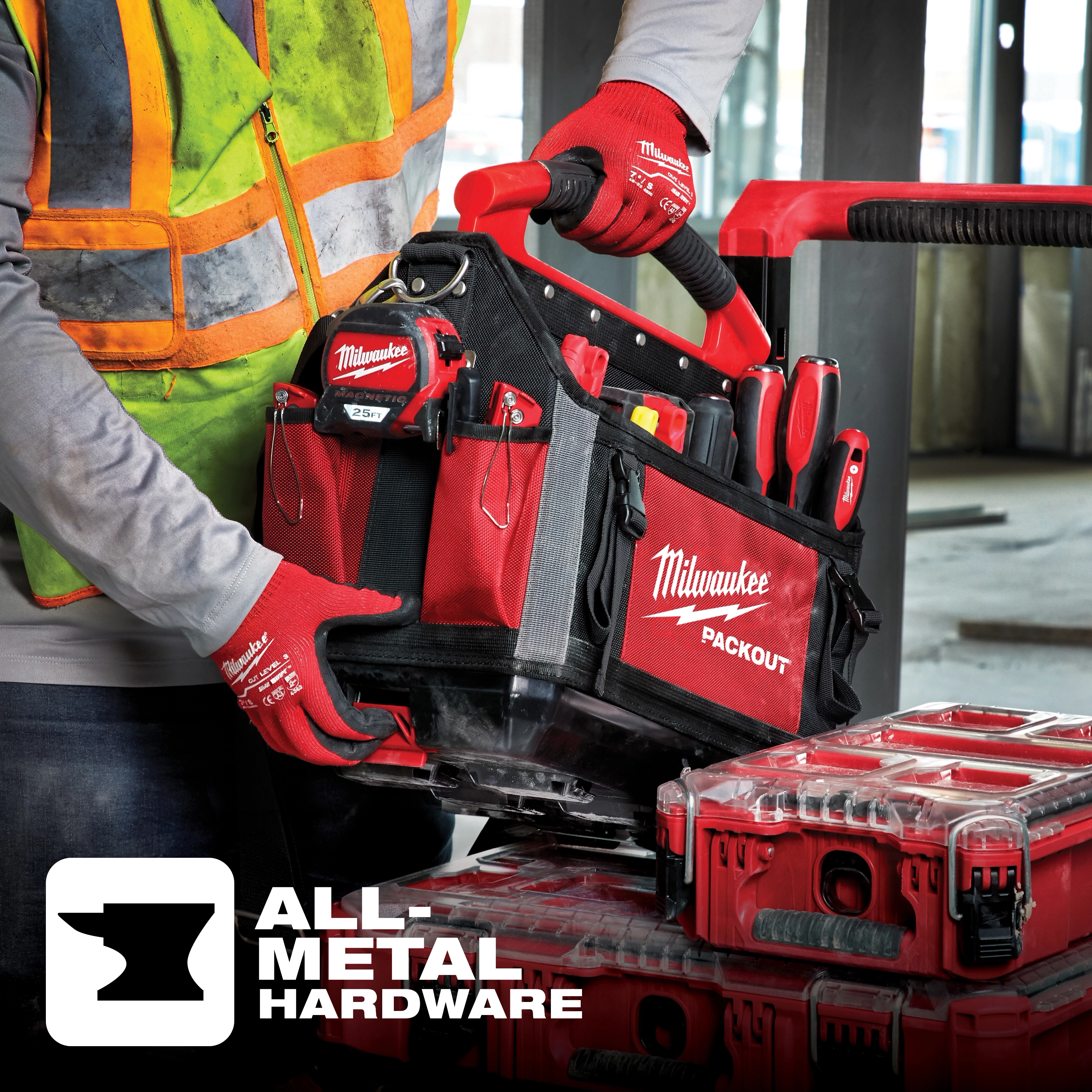 A construction worker with gloves is holding a Milwaukee PACKOUT tool bag, demonstrating its all-metal hardware feature.