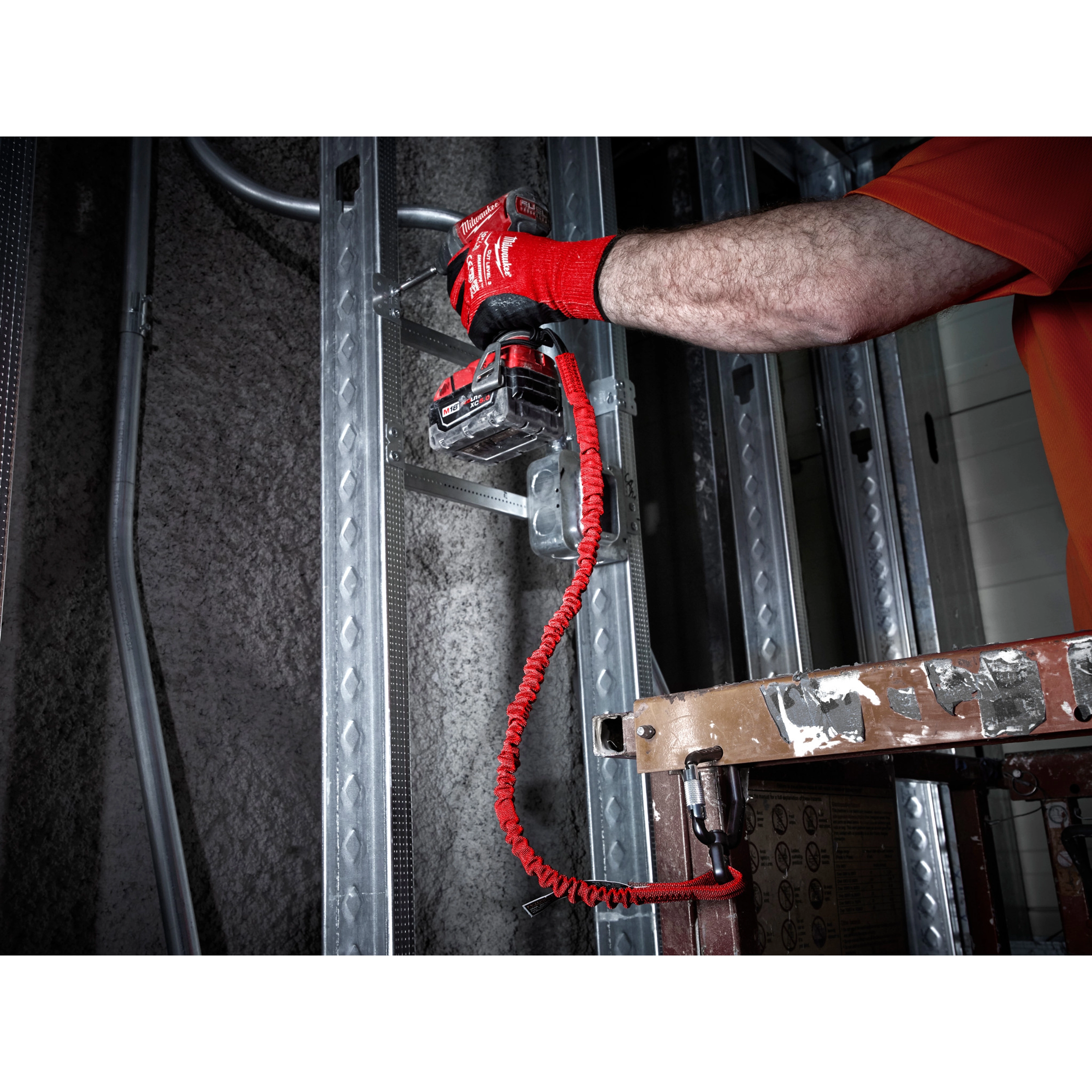 Worker using a red 5 LB Locking Tool Lanyard to secure a power tool while installing metal framing on a construction site.