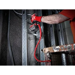 Worker using a red 5 LB Locking Tool Lanyard to secure a power tool while installing metal framing on a construction site.