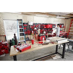 Workshop with a wall-mounted system showcasing the PACKOUT Large Wall Plate, holding various red and black tools and storage bins.