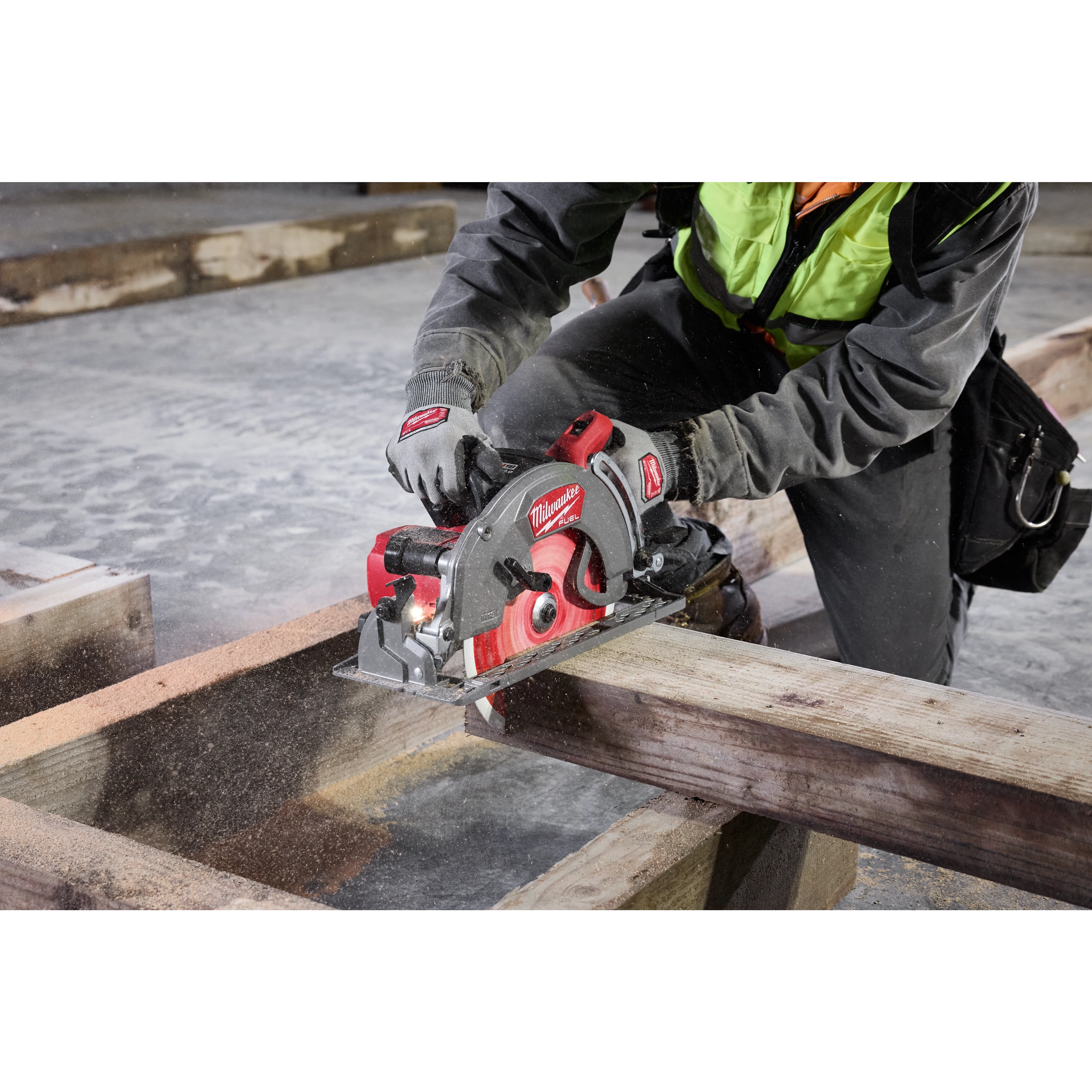 Worker uses the M18 FUEL Rear Handle Circular Saw to cut a wooden beam. The saw produces visible sawdust. Worker wears safety gear.