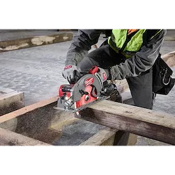 Worker uses the M18 FUEL Rear Handle Circular Saw to cut a wooden beam. The saw produces visible sawdust. Worker wears safety gear.