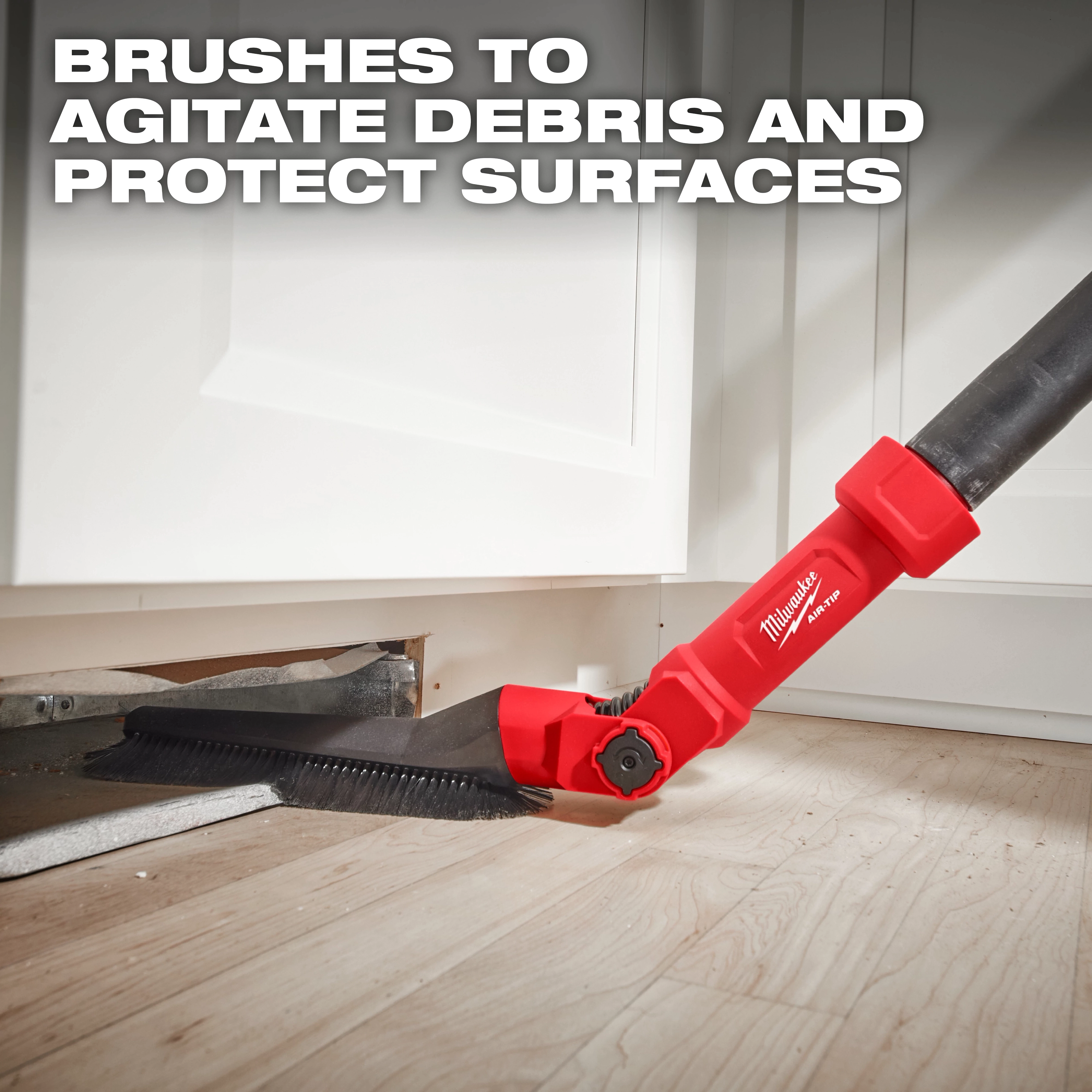 The image shows the AIR-TIP™ Low-Profile Pivoting Brush Tool being used to clean under kitchen cabinets. The tool is red with black bristles and designed to agitate debris and protect surfaces, as stated in the text "BRUSHES TO AGITATE DEBRIS AND PROTECT SURFACES."