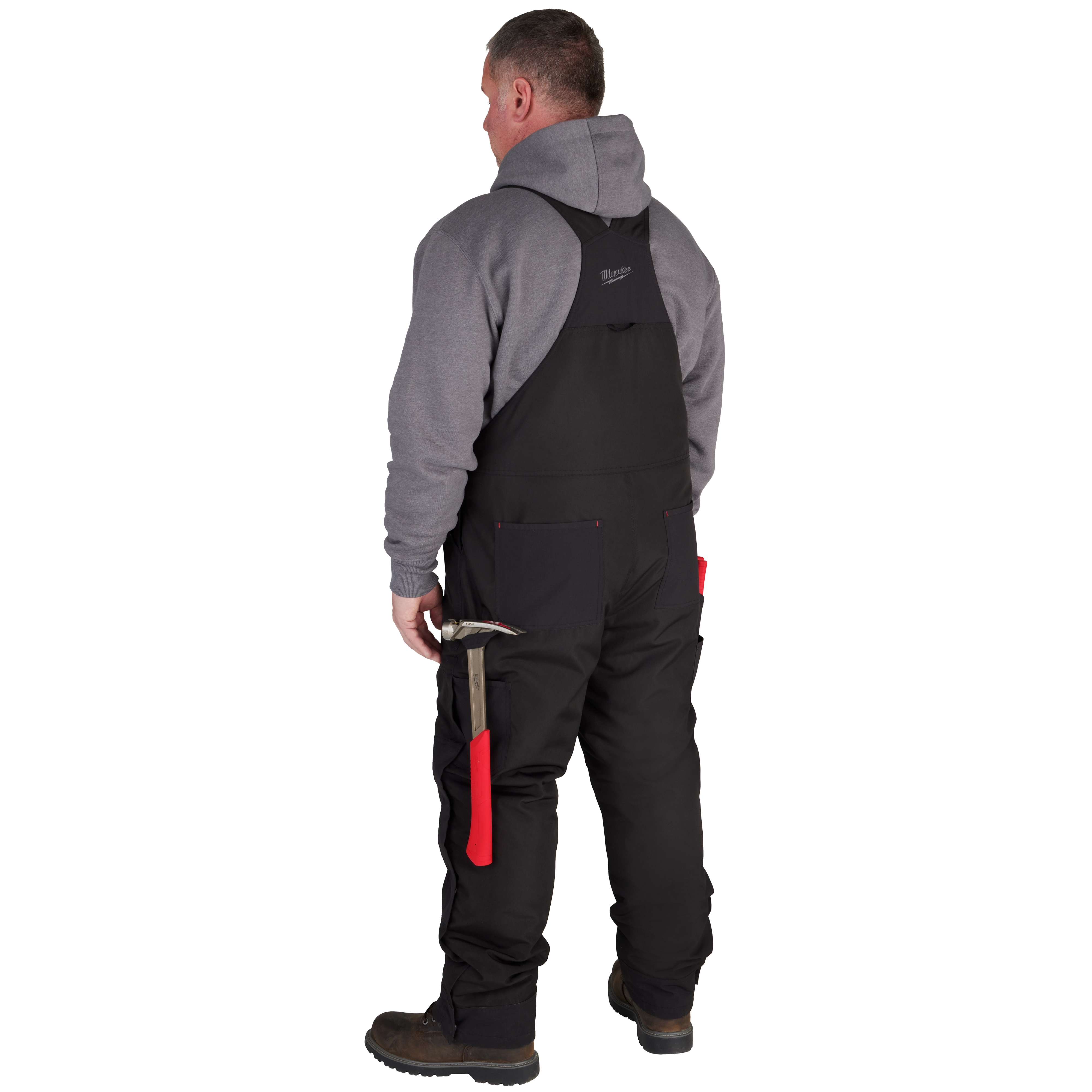 Man wearing FREEFLEX Insulated Bib Overalls in black, grey hoodie, while holding a hammer with a red handle, standing outdoors.
