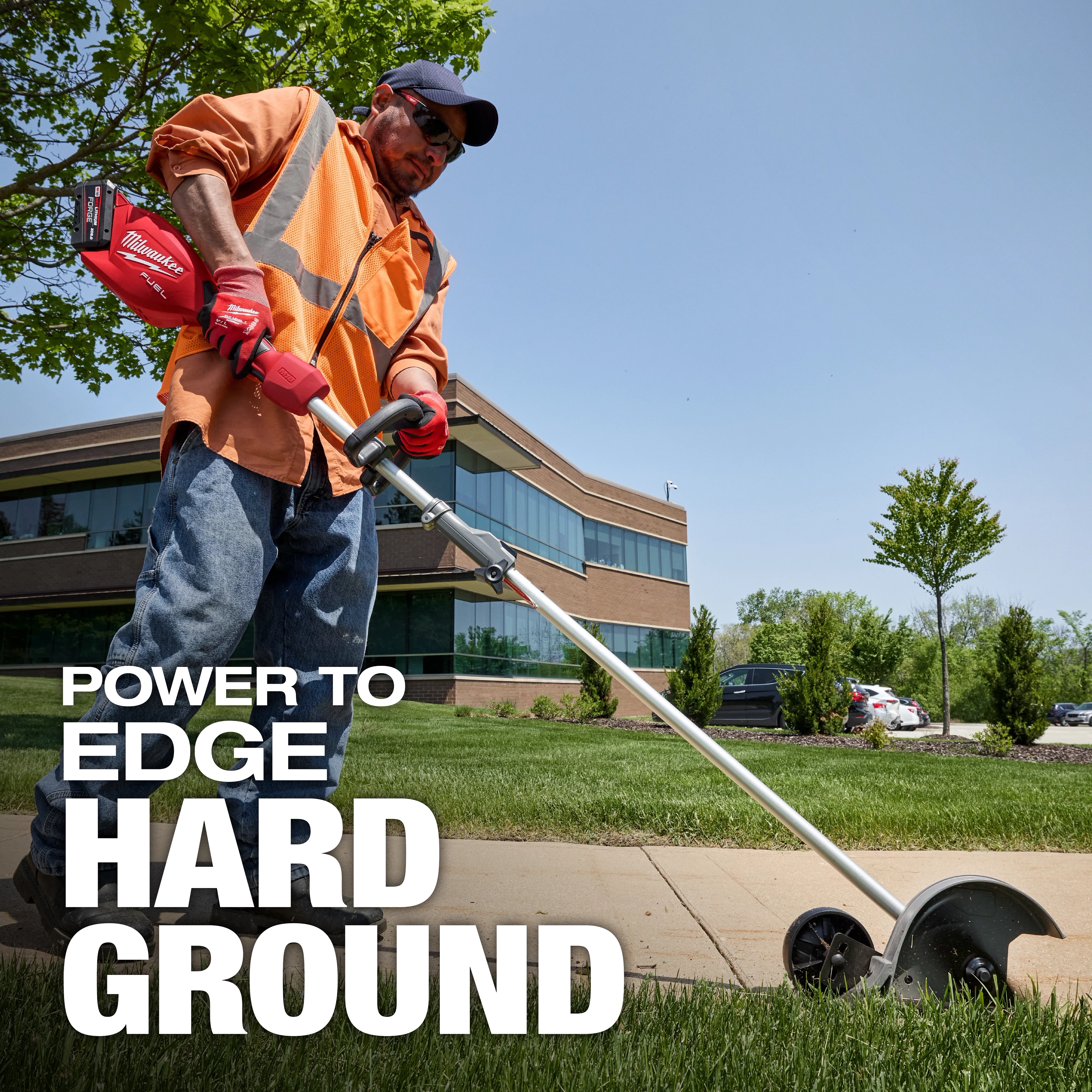 Worker using an M18 FUEL QUIK-LOK Edger Attachment to edge grass along a sidewalk near an office building.