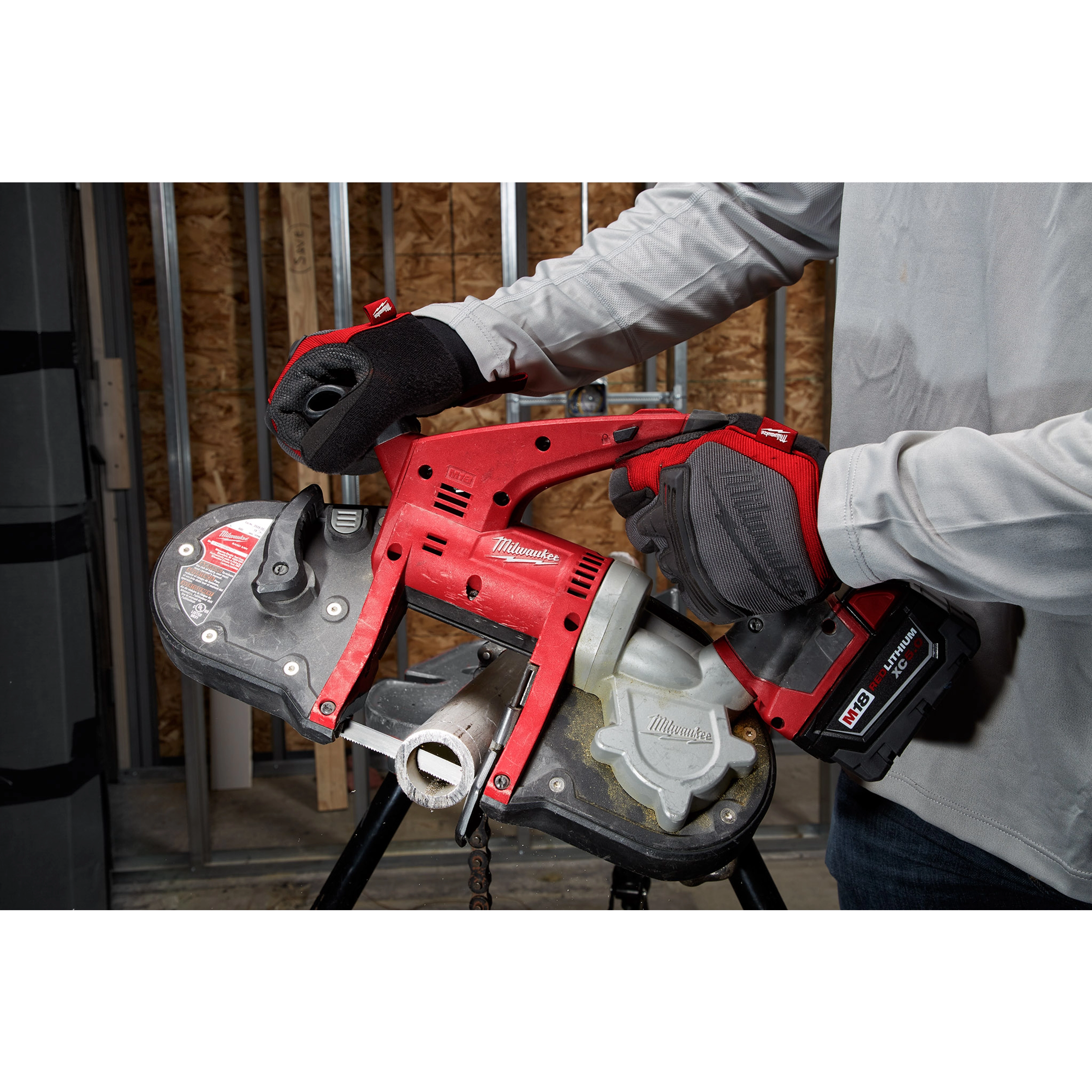 Person using a red Compact Extreme Thick Band Saw Blade to cut a pipe in a construction area, wearing gloves and a light-colored shirt.