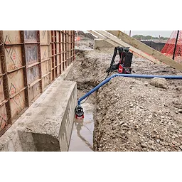 An MX FUEL™ Portable Pump Power Base and an MX FUEL™ 1HP 2" Submersible Pump Kit in use at a construction site. The submersible pump is placed in a water-filled trench, connected to the power base via a blue hose.