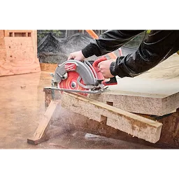 A person cutting plywood with the M18 FUEL 10-1/4" Rear Handle Circular Saw, creating sawdust and precise cuts on a construction site.