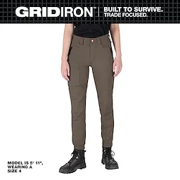 A woman is wearing Women's GRIDIRON Double Knee Jogger Pants in brown. The model is 5' 11" and is wearing a size 4. The pants feature multiple pockets and reinforced knee panels. The brand slogan "BUILT TO SURVIVE. TRADE FOCUSED." is displayed at the top.