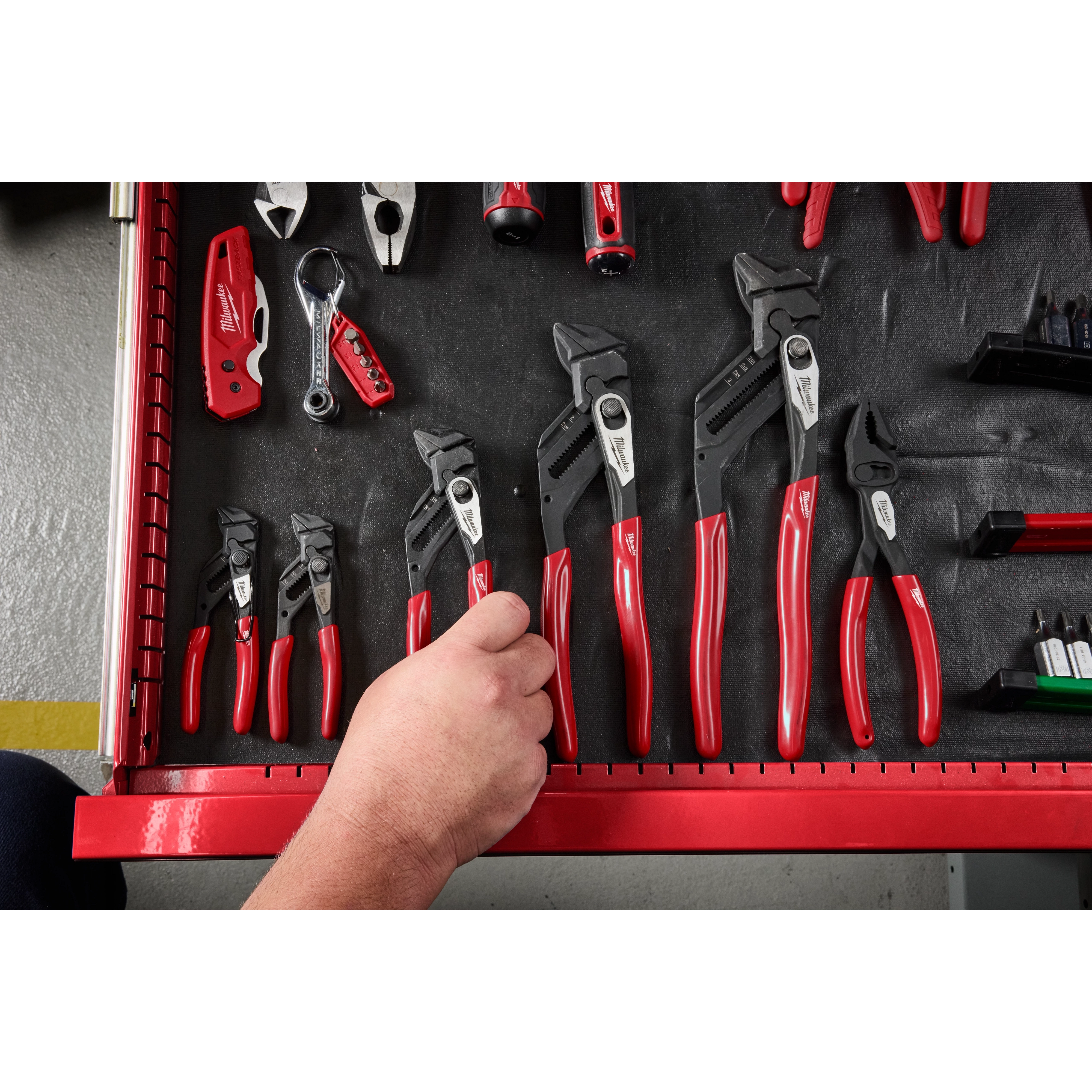 A hand reaches into a red toolbox drawer that contains various sizes of Pliers and Wrenches, all part of a family featuring black metal heads and red handles.