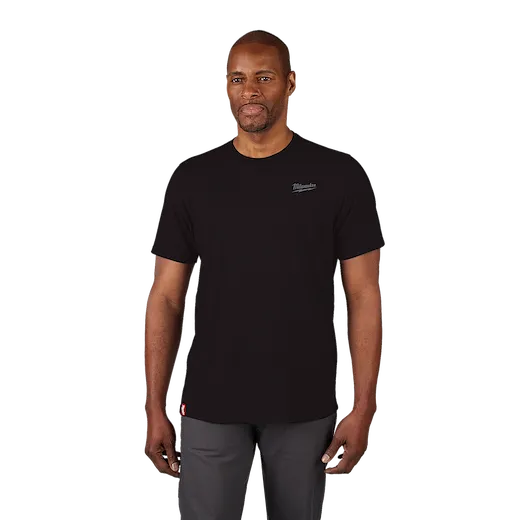 Man wearing a black Hybrid Work Tee with short sleeves, small logo on upper left chest, and red tag near hem, paired with gray pants.