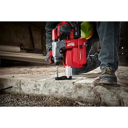 Worker using a red SDS+ MX4 1/2" X 4" X 6" rotary hammer drill to bore into a concrete surface at a construction site.