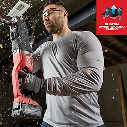 Person wearing WORKSKIN Lightweight Performance Shirt - Long Sleeve holding a power tool surrounded by wood shavings. Custom sweat-wicking fabric.