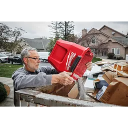 A man empties debris from a 9 Gallon Wet/Dry Vacuum Tank into a large outdoor trash bin in a residential area.