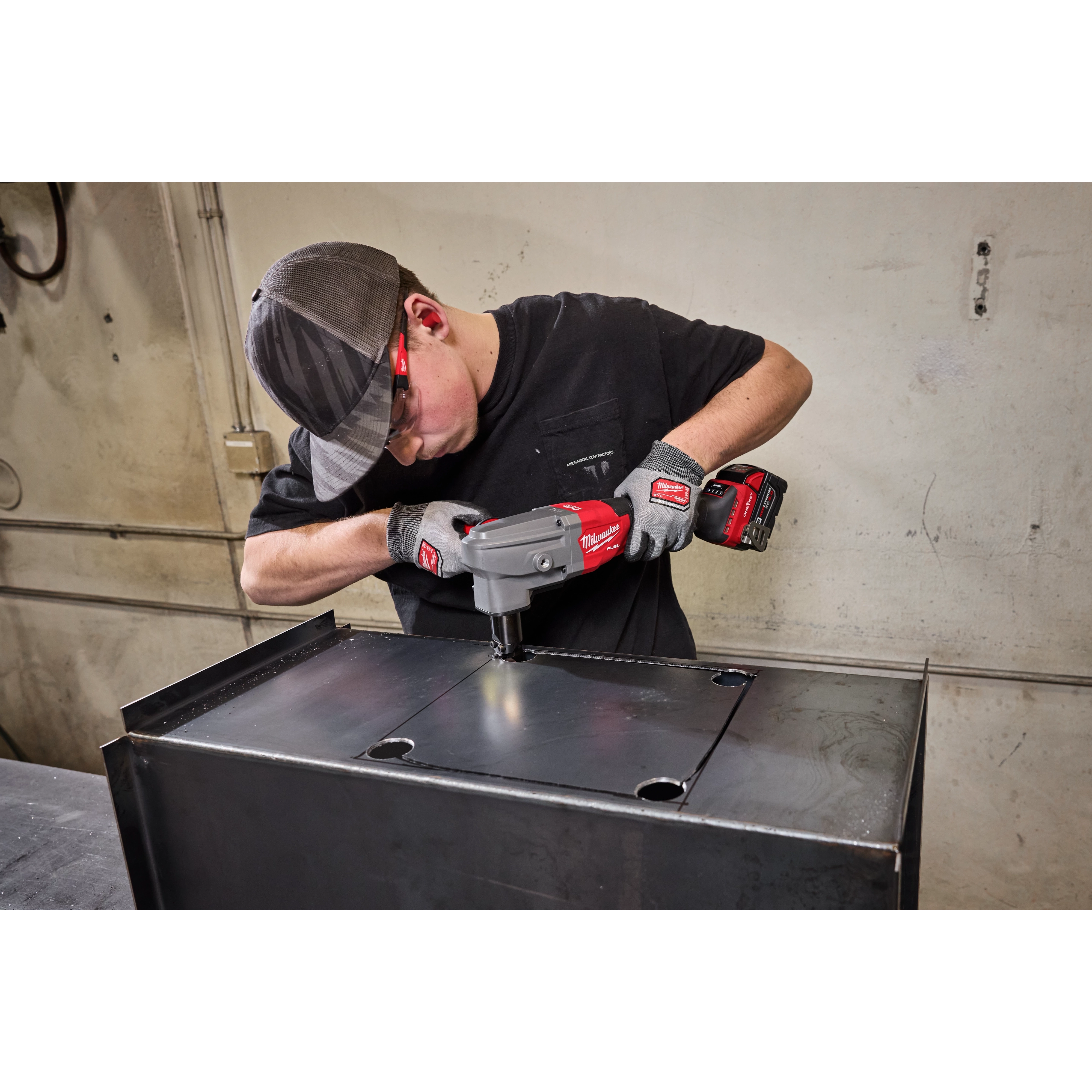 A man wearing safety gear uses an M18 FUEL™ 10 Gauge Nibbler to cut a metal sheet. The cordless tool is branded in red and is designed for precise cuts in heavy gauge materials.