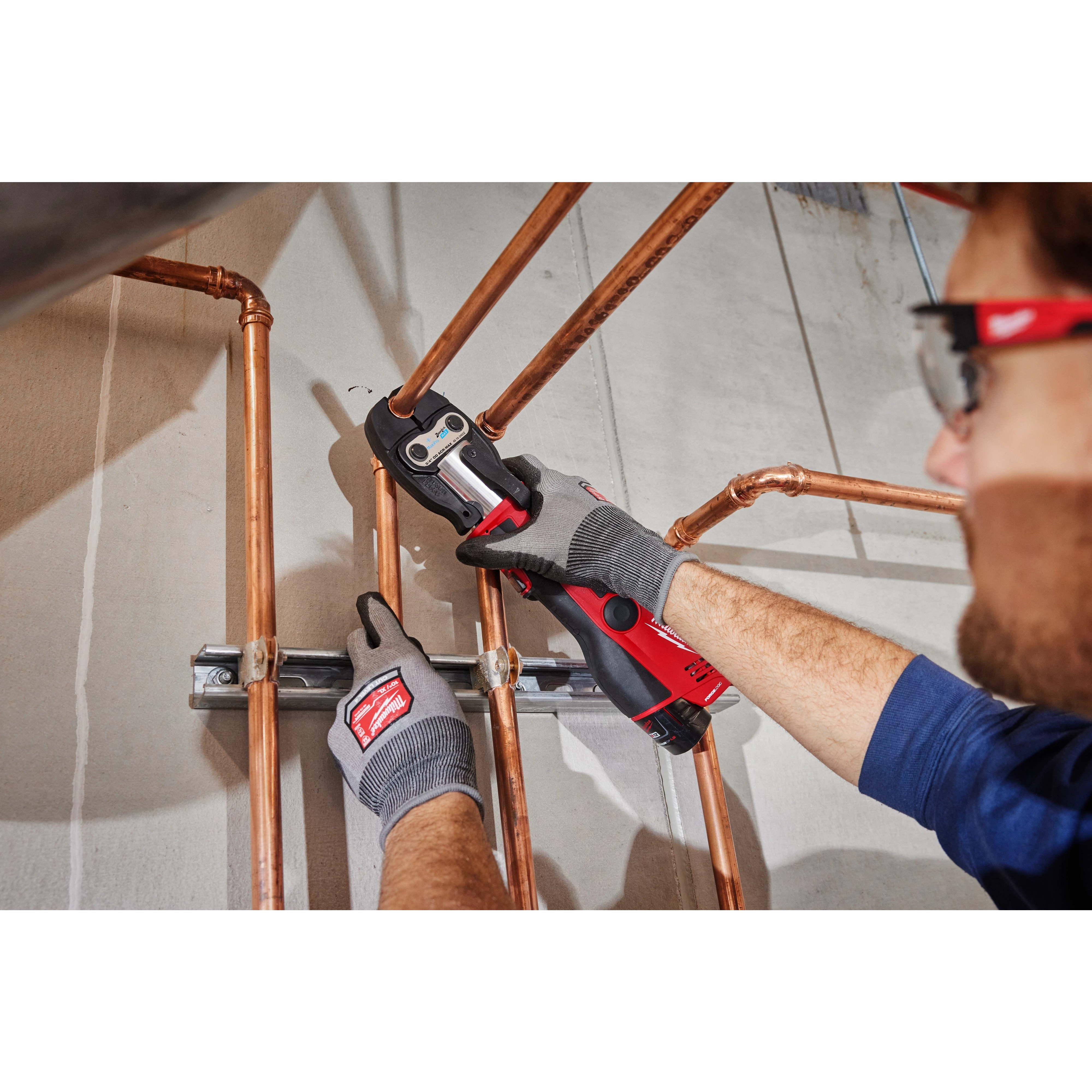 A person using a 1-1/8" ZoomLock MAX Press Jaw for M12 FORCE LOGIC Press Tools to press copper pipes during installation.