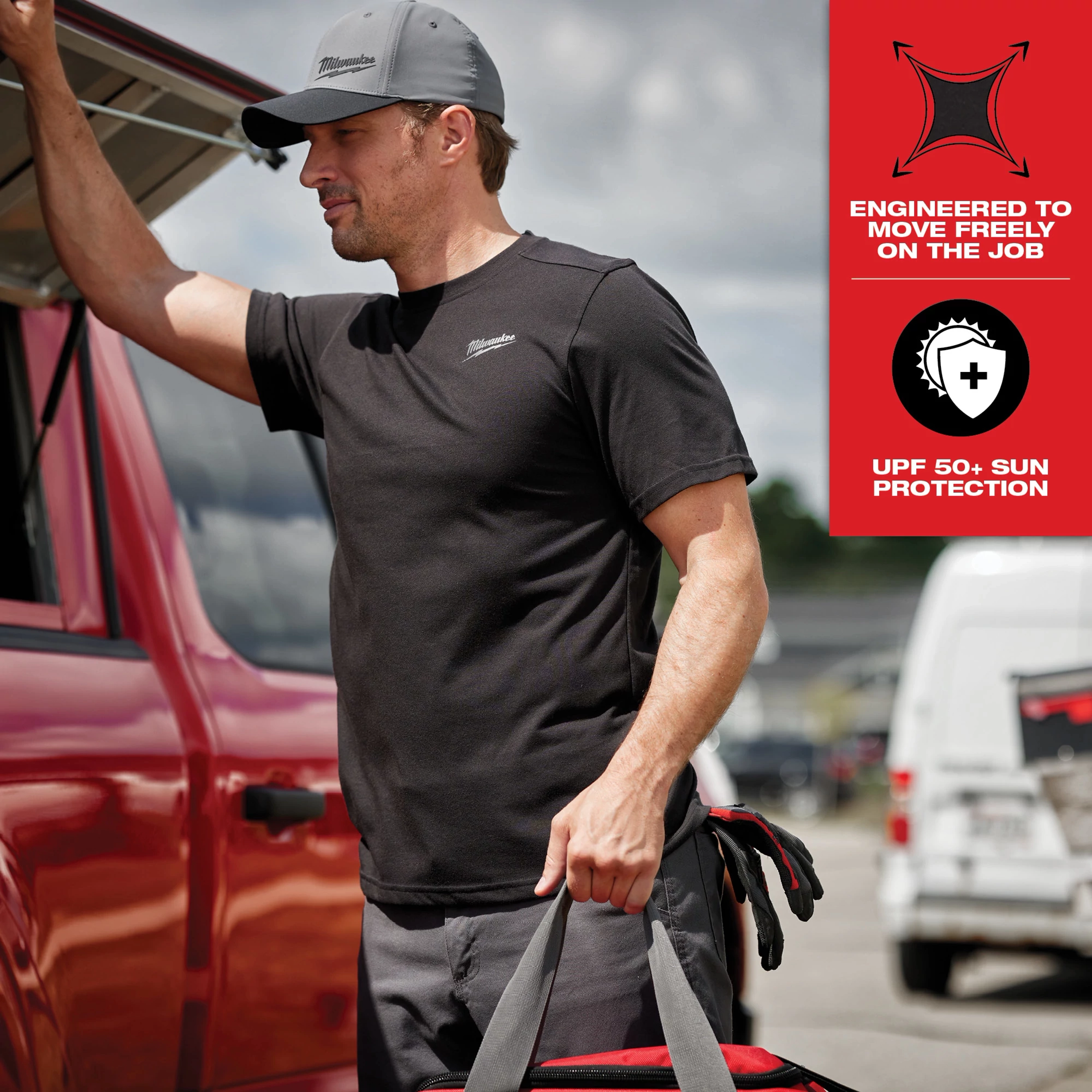 Man wearing black Hybrid Work Tee - Short Sleeve Feature Shot, standing by a red vehicle and holding a bag. Shirt provides UPF 50+ sun protection.