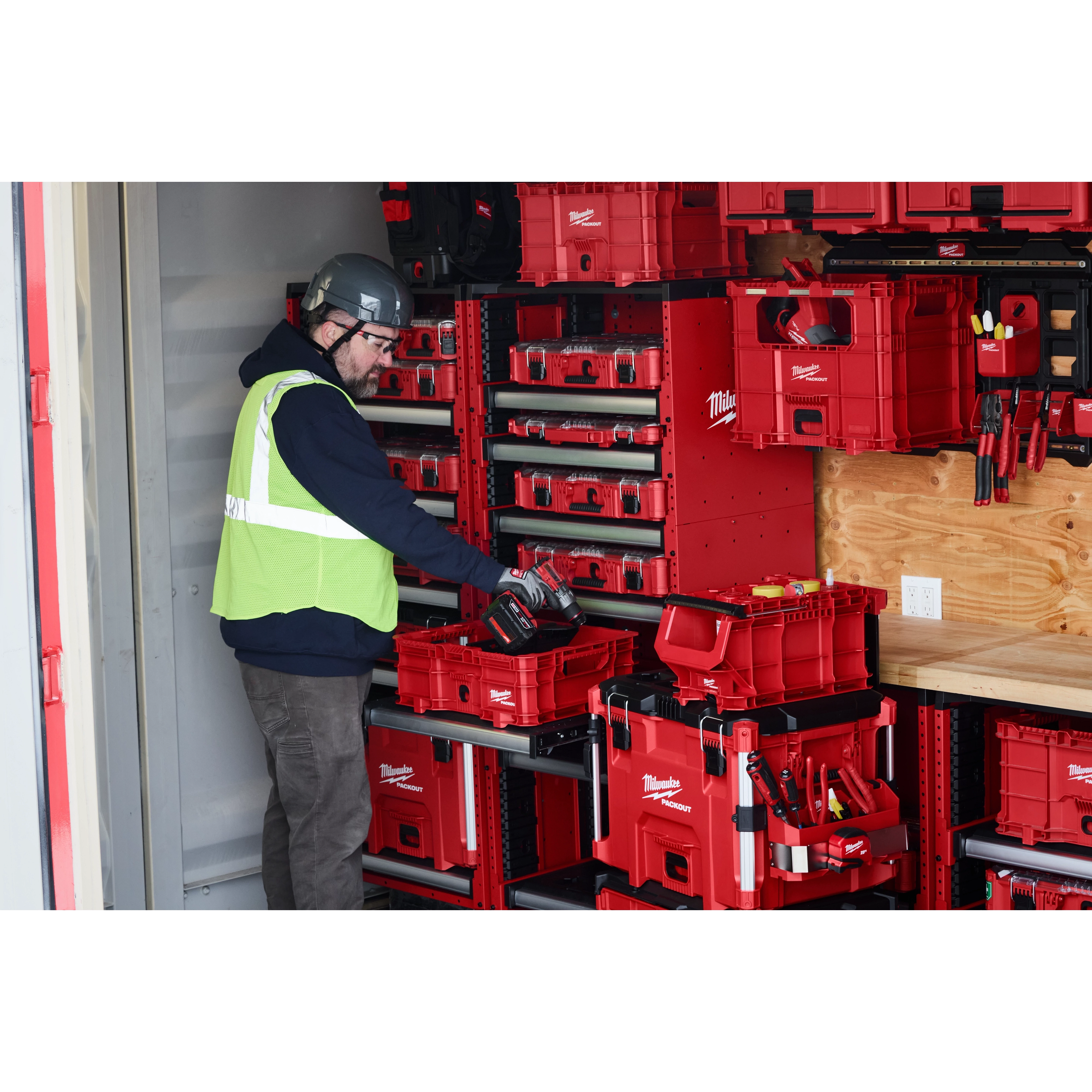 Worker organizing PACKOUT Low-Profile Crate, PACKOUT Compact Crate, and PACKOUT XL Crate in a storage unit equipped with shelving.