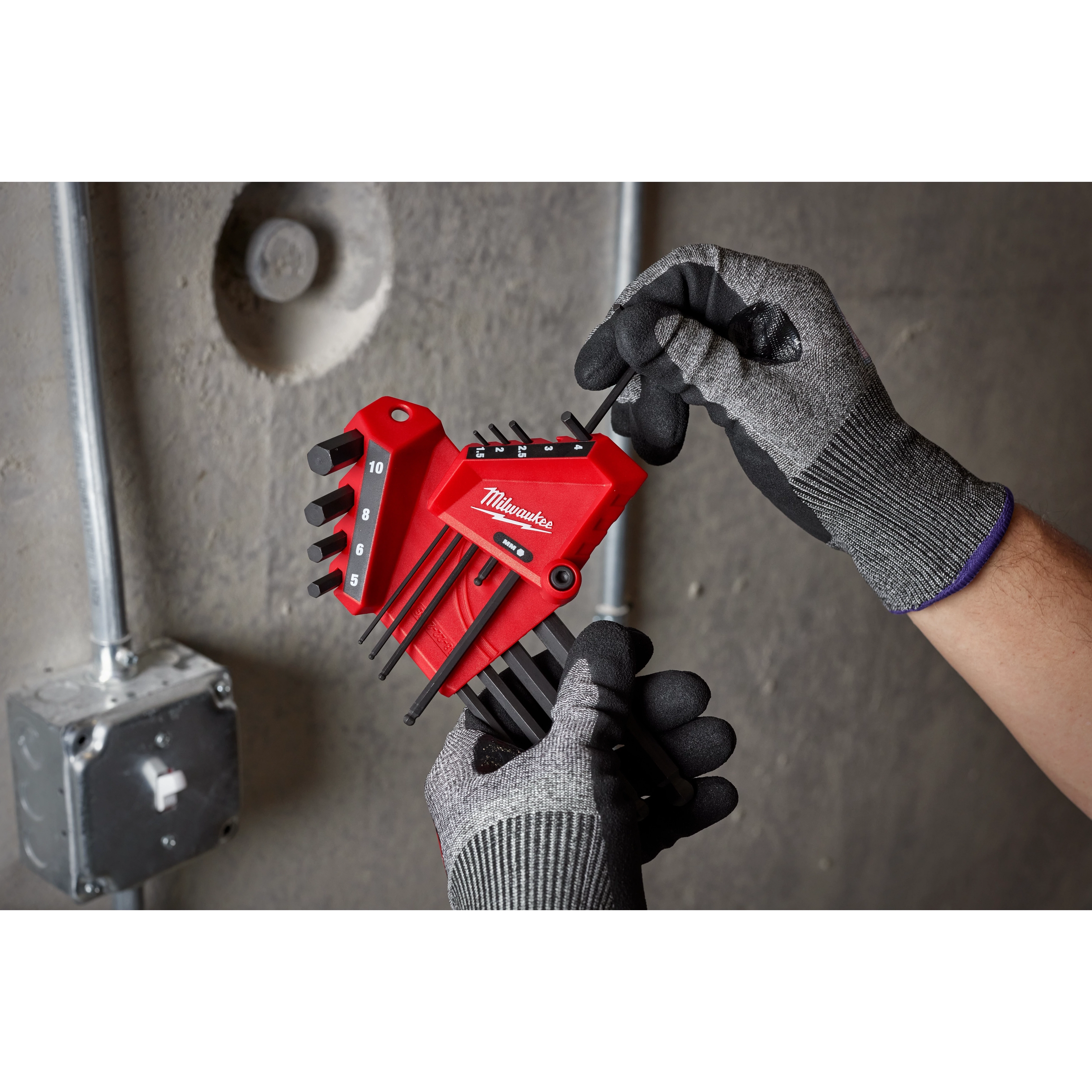 Gloved hands hold the 9-Key Ball End L-Key Set - Metric in front of a concrete wall with visible electrical conduit.
