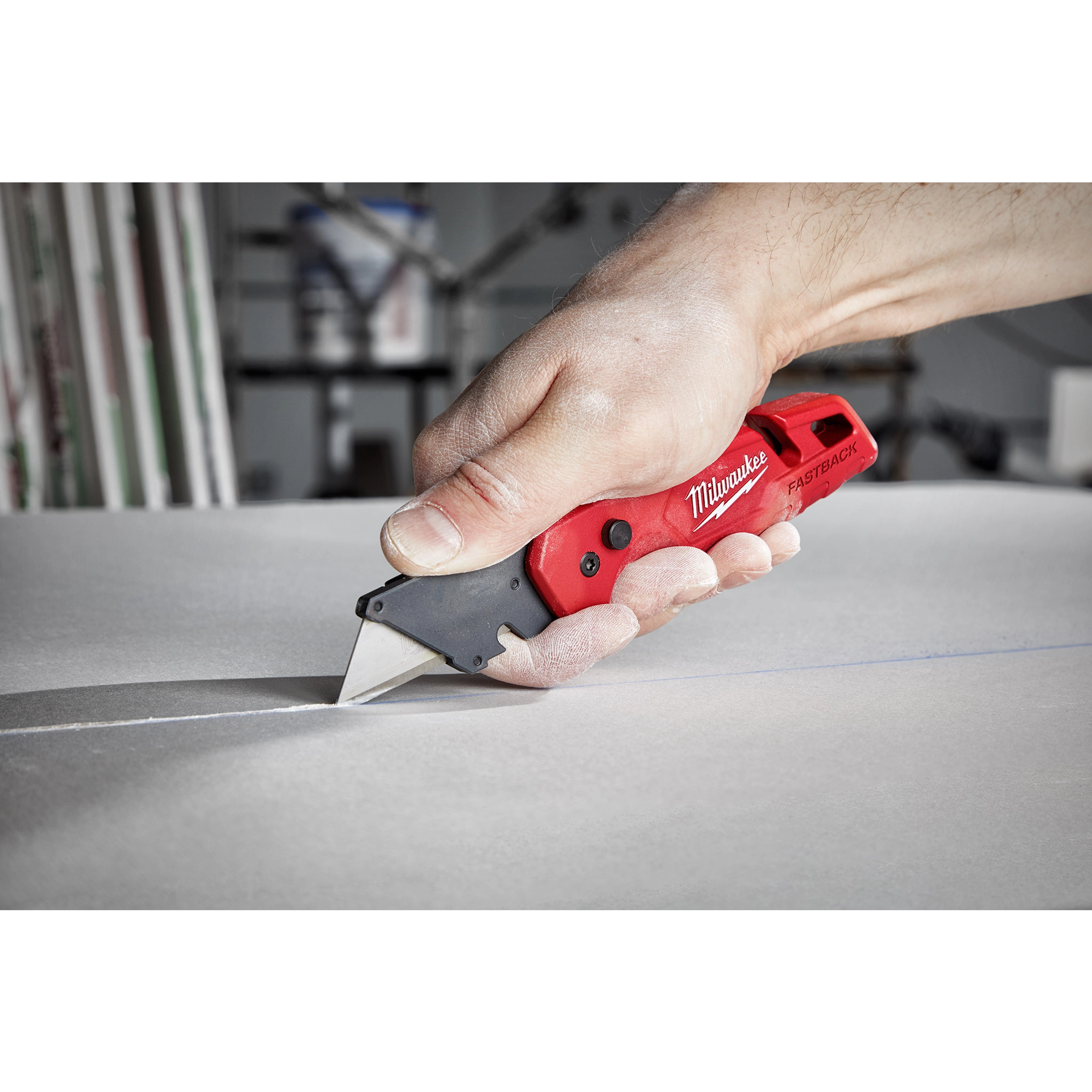 A person cutting a white material using a red FASTBACK Folding Utility Knife, with the knife held in their right hand.