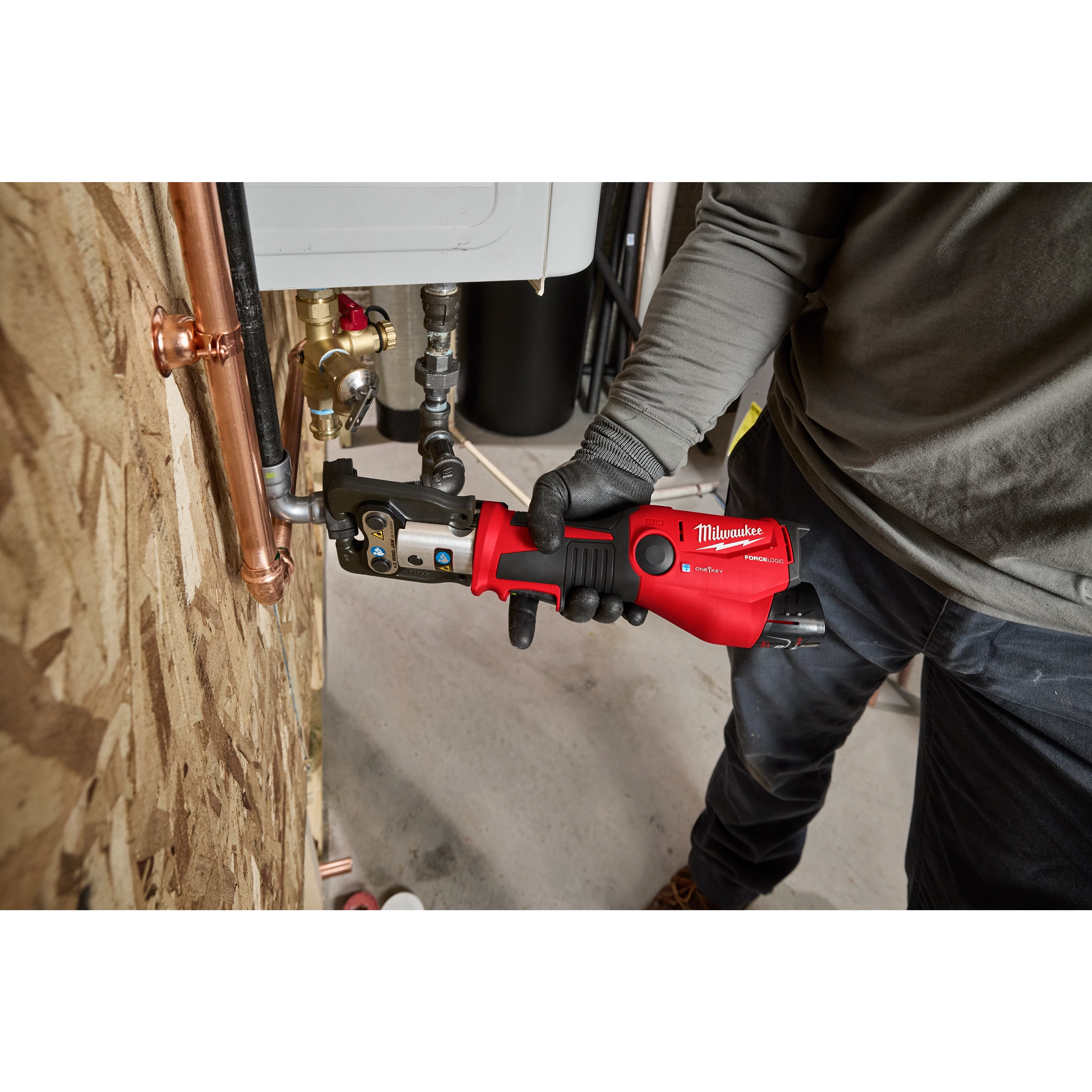 M12 FORCE LOGIC Press Tool Kit with ONE-KEY being used to press a fitting on a copper pipe by a person wearing work clothes.