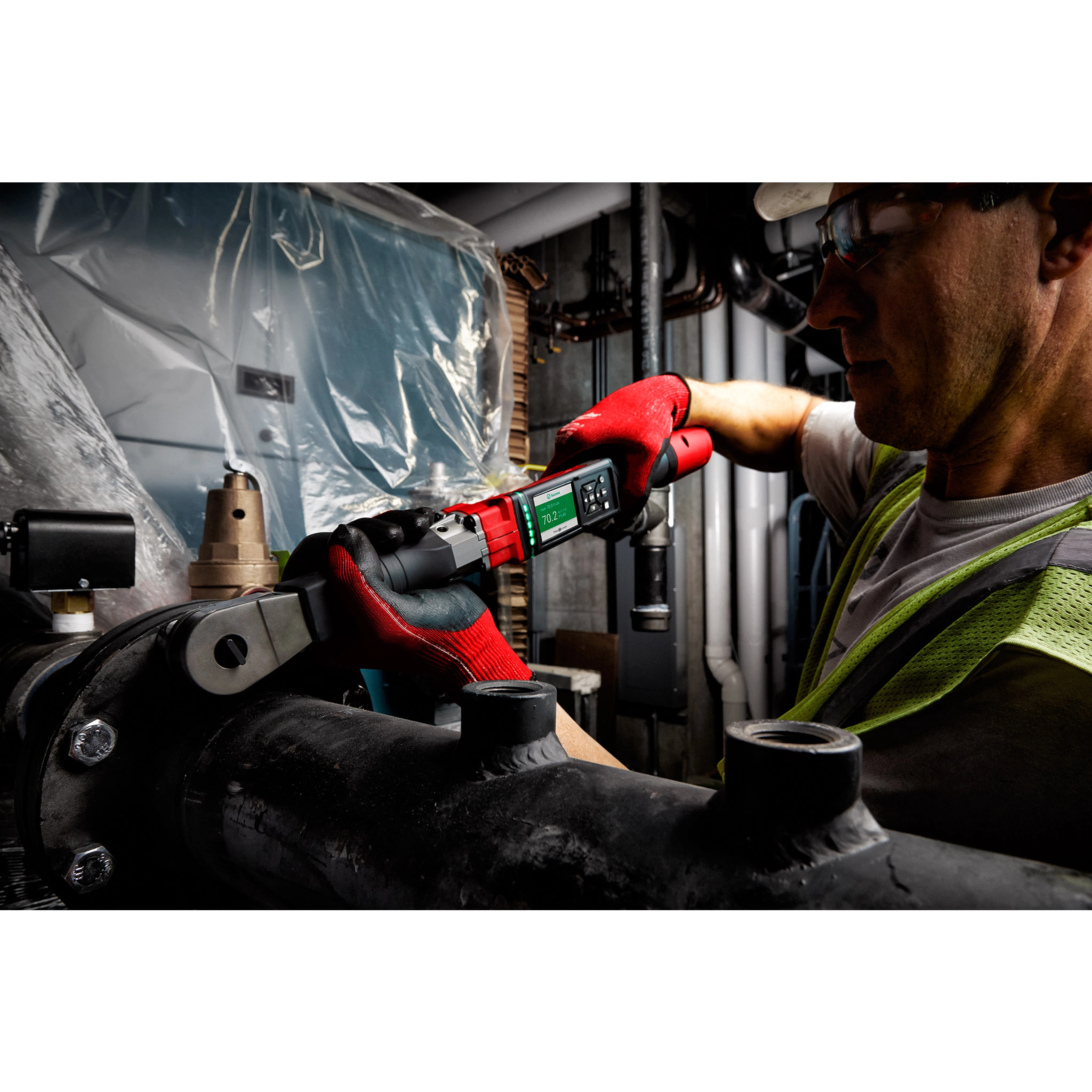 Worker using the M12 FUEL 1/2" Digital Torque Wrench with ONE-KEY App Shot to tighten a pipe fitting in an industrial setting.
