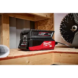 Milwaukee MX Fuel Redlithium battery charger on a wooden surface, with a charging indicator and a saw blade in the background.