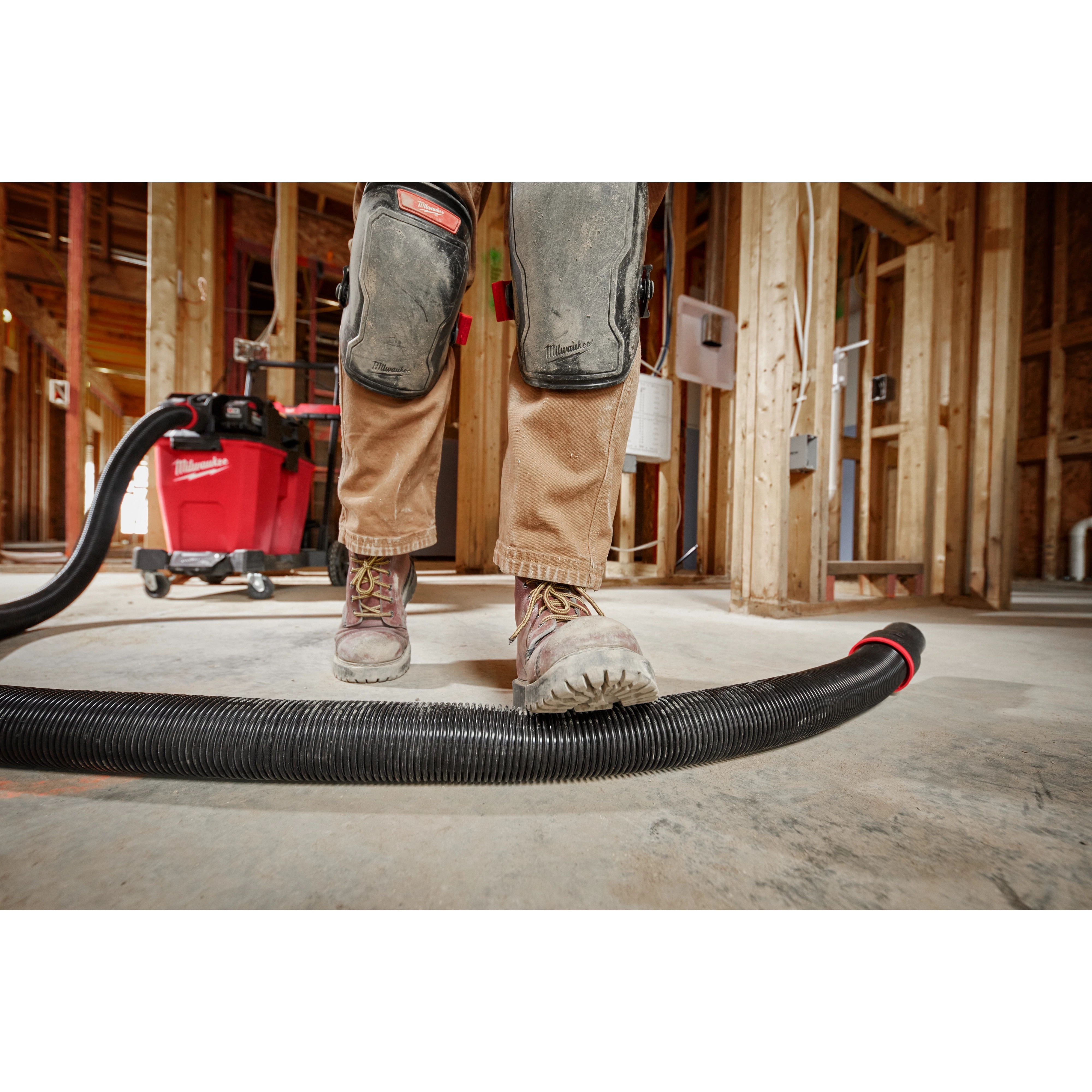 Worker standing on a 2-1/2” x 9' Flexible Hose in a construction site. A red vacuum is in the background.
