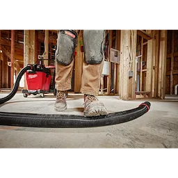 Worker standing on a 2-1/2” x 9' Flexible Hose in a construction site. A red vacuum is in the background.