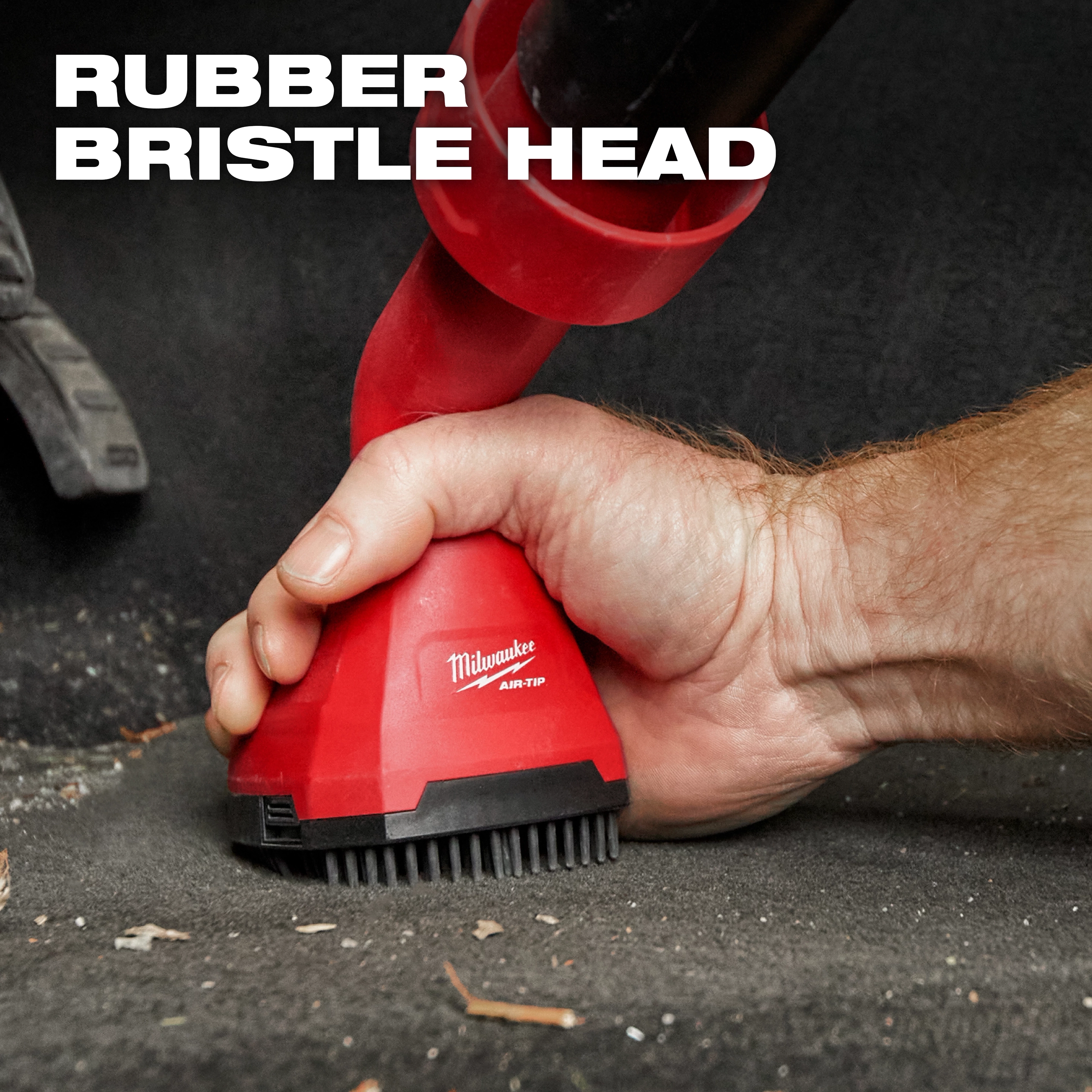 A person grips the AIR-TIP™ Swiveling Palm Brush with a rubber bristle head, ideal for cleaning. The red brush features the Milwaukee logo and is designed for easy handling. The text "RUBBER BRISTLE HEAD" is displayed at the top left of the image.