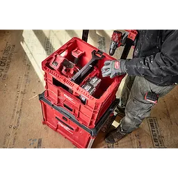 Person using a Divider for PACKOUT XL Crate to organize red tool containers on a construction site.