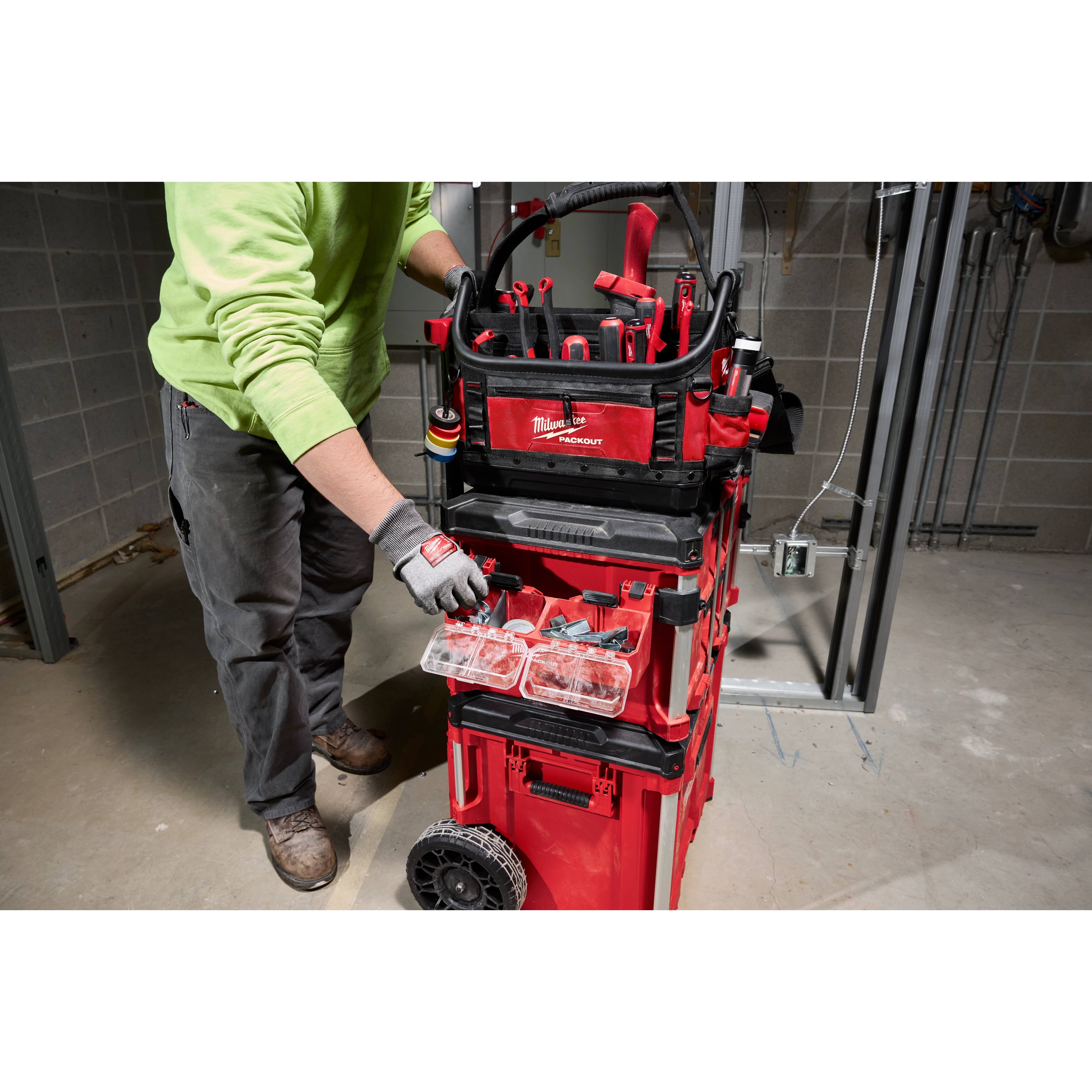 Person using PACKOUT Tool Box 2-Bin Attachment in a construction setting. The tool box is red with multiple compartments and tools.