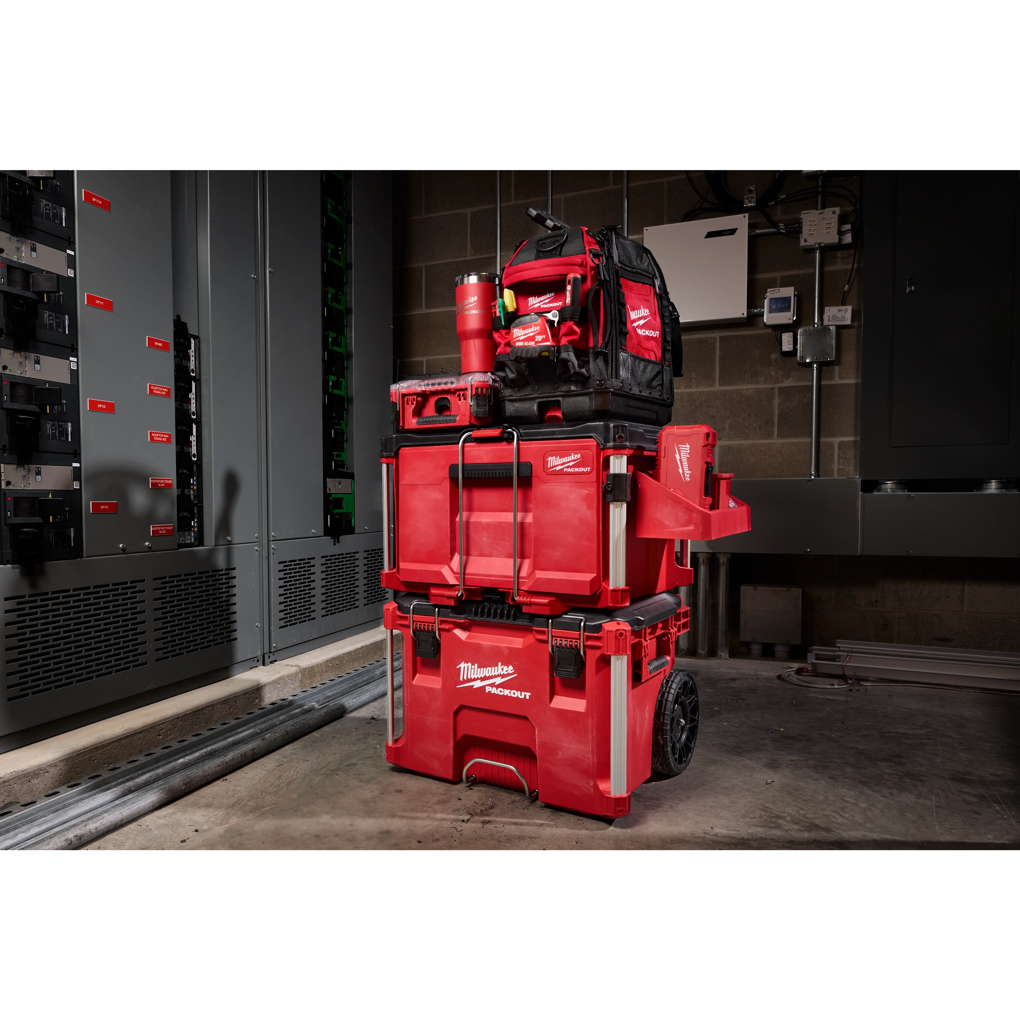 Milwaukee Packout rolling tool chest stacked with tool boxes and a backpack in an industrial room.