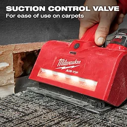A hand using the red M12™ AIR-TIP™ Utility Nozzle on a carpet. The nozzle has a suction control valve for ease of use on carpets. A partially exposed wall is visible in the background. Text on the image highlights the suction control valve feature.