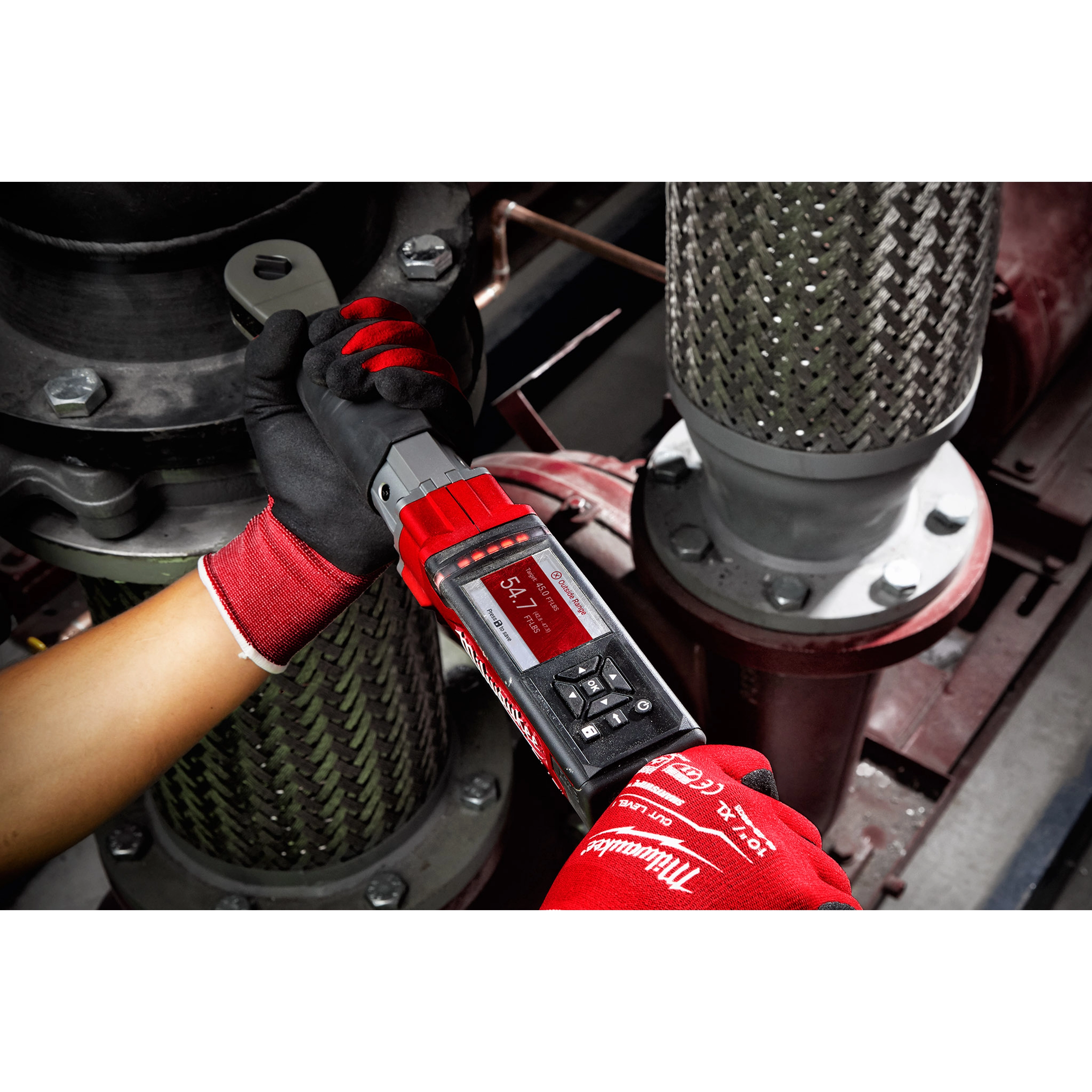 A person wearing red gloves uses an M12 FUEL 1/2” Digital Torque Wrench with ONE-KEY App Shot to tighten a bolt in an industrial setting.